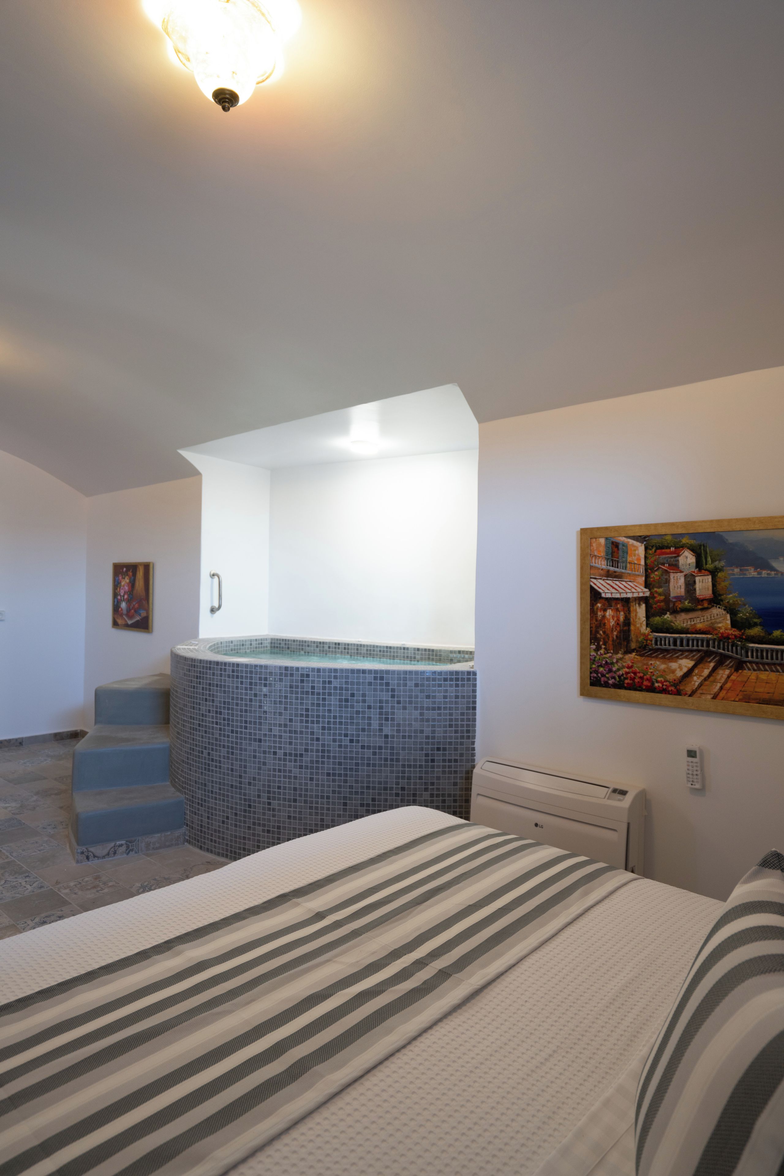 A hotel room with a bed, a painting, a tiled bathroom, and a staircase leading to a balcony.