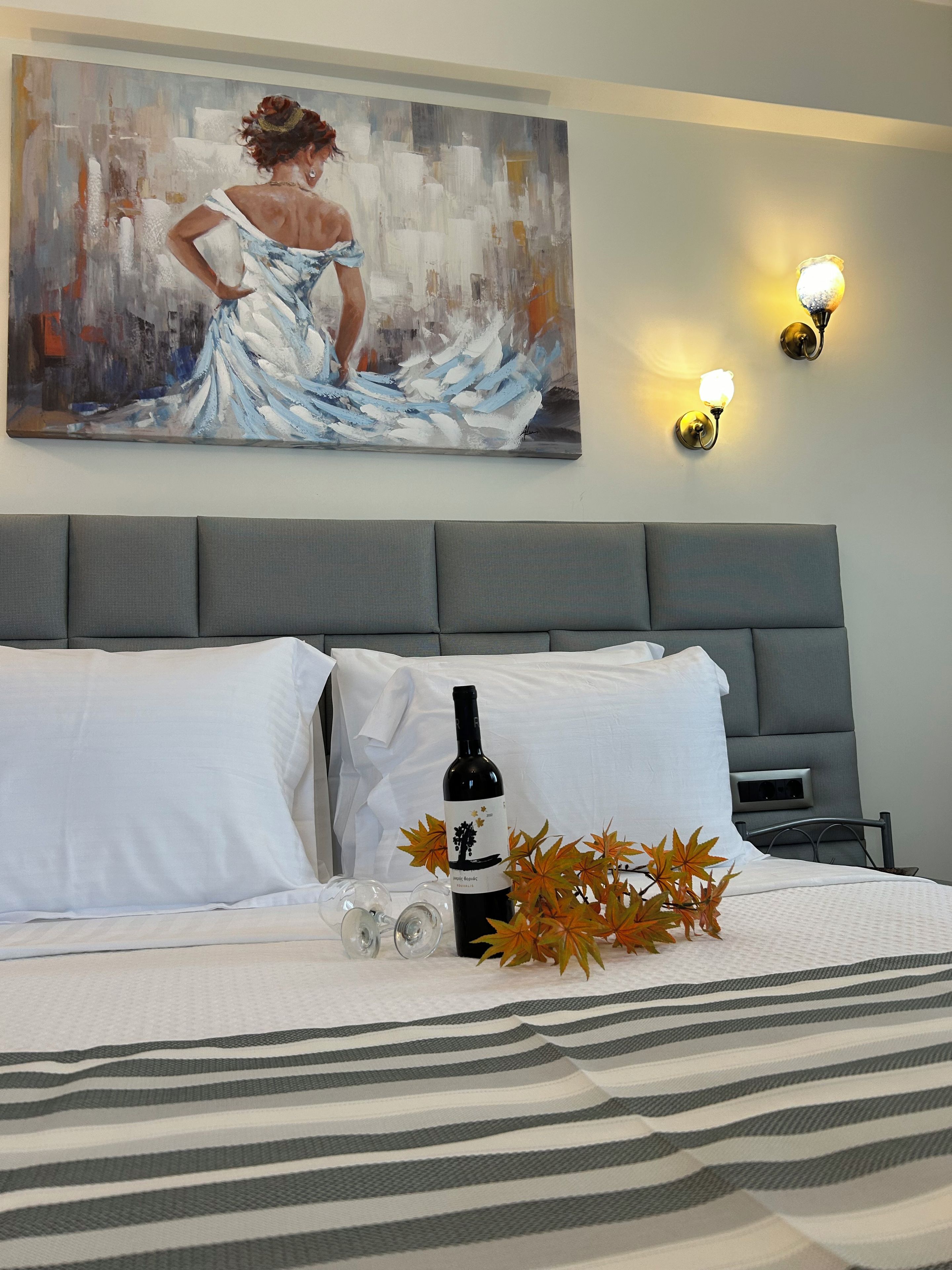 A hotel room with a bed, a painting on the wall, and a bottle of wine on the bed.