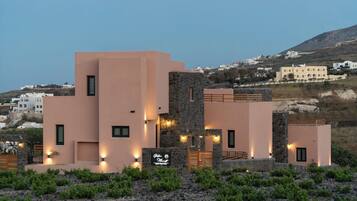 A modern building with multiple levels and a stone facade, surrounded by greenery and set against a hilly backdrop.