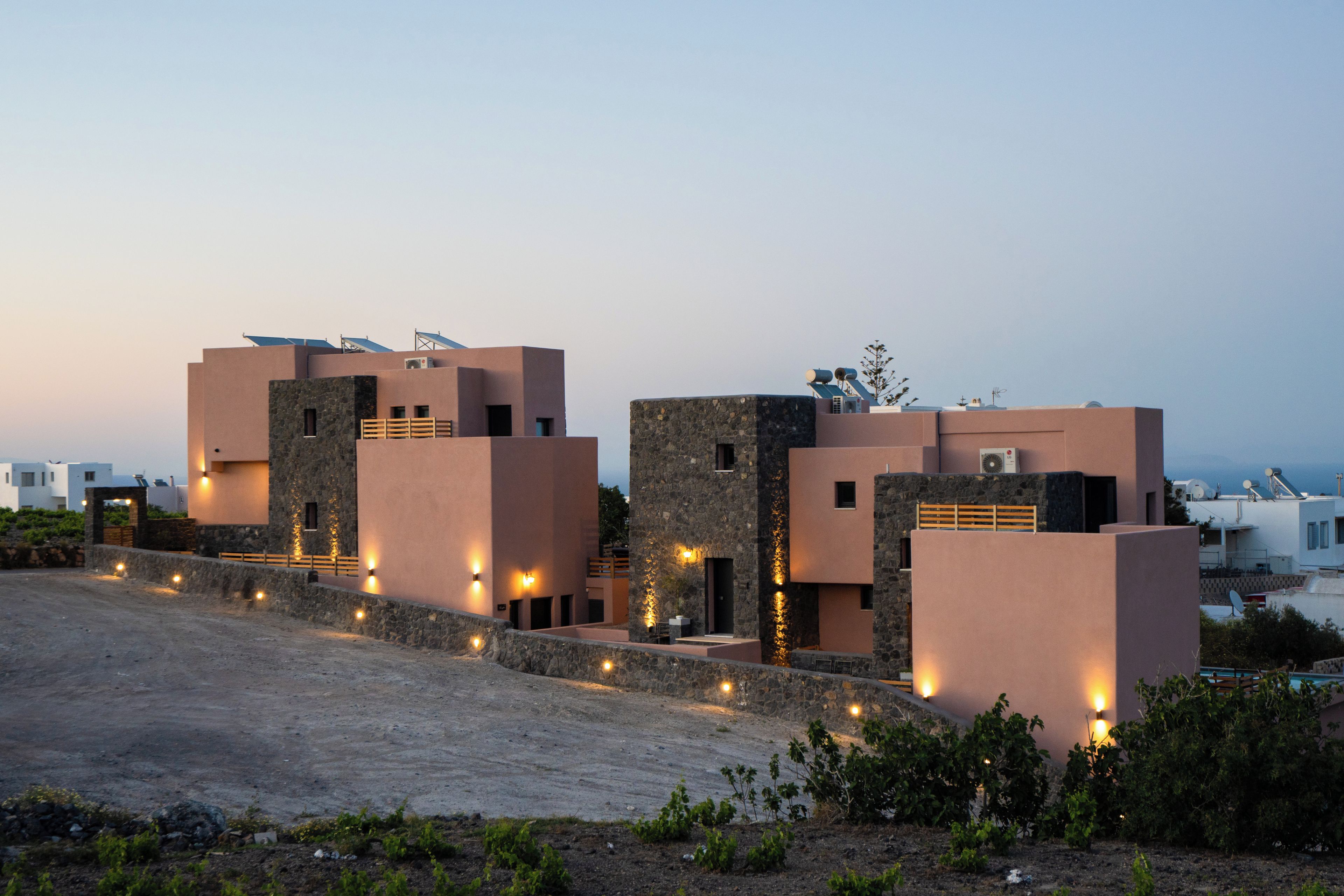 A modern building with multiple levels and a flat roof, featuring solar panels and outdoor lighting.