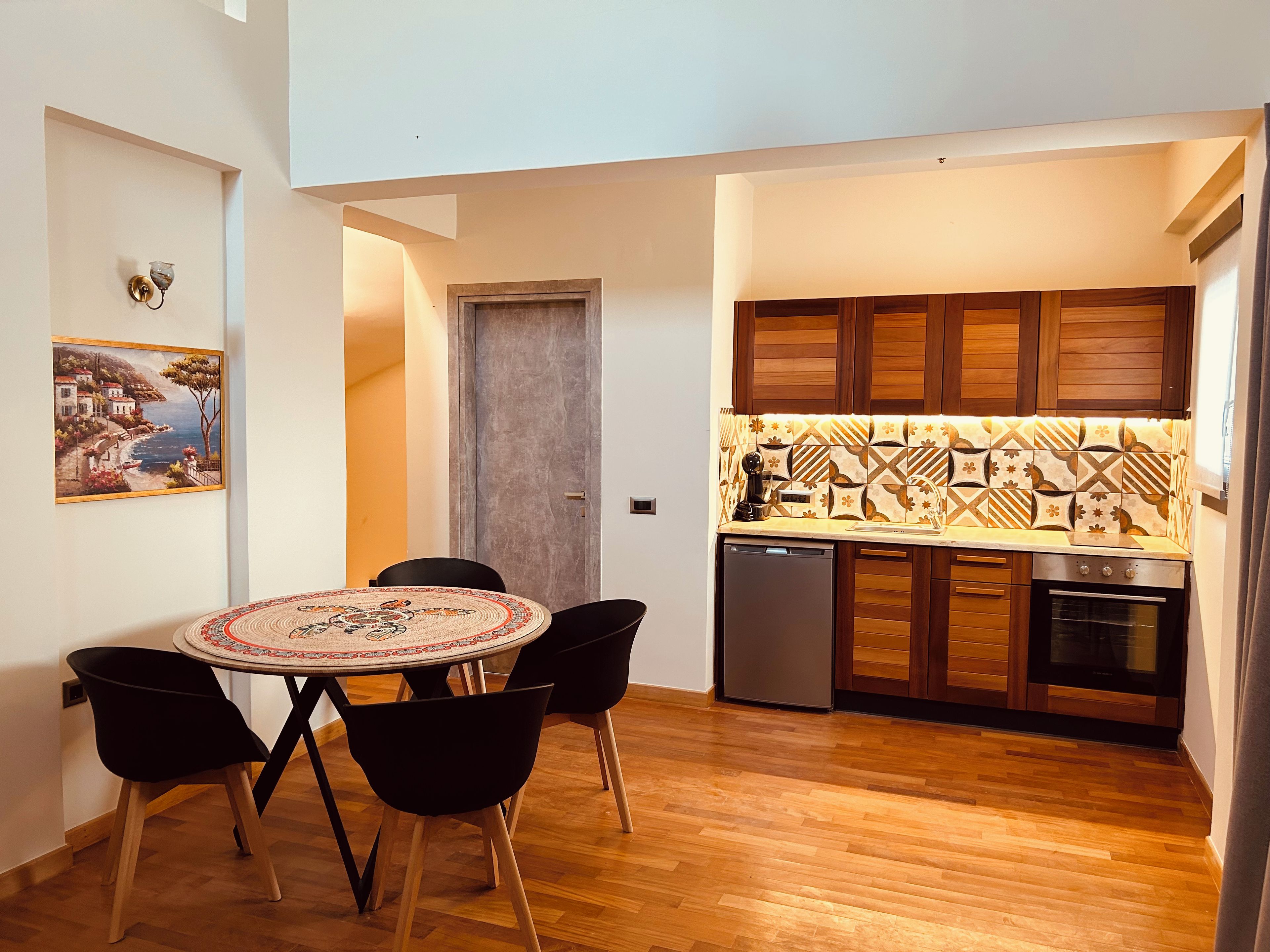 A compact kitchen with wooden cabinets, a tiled backsplash, and a dining area with a round table and chairs.