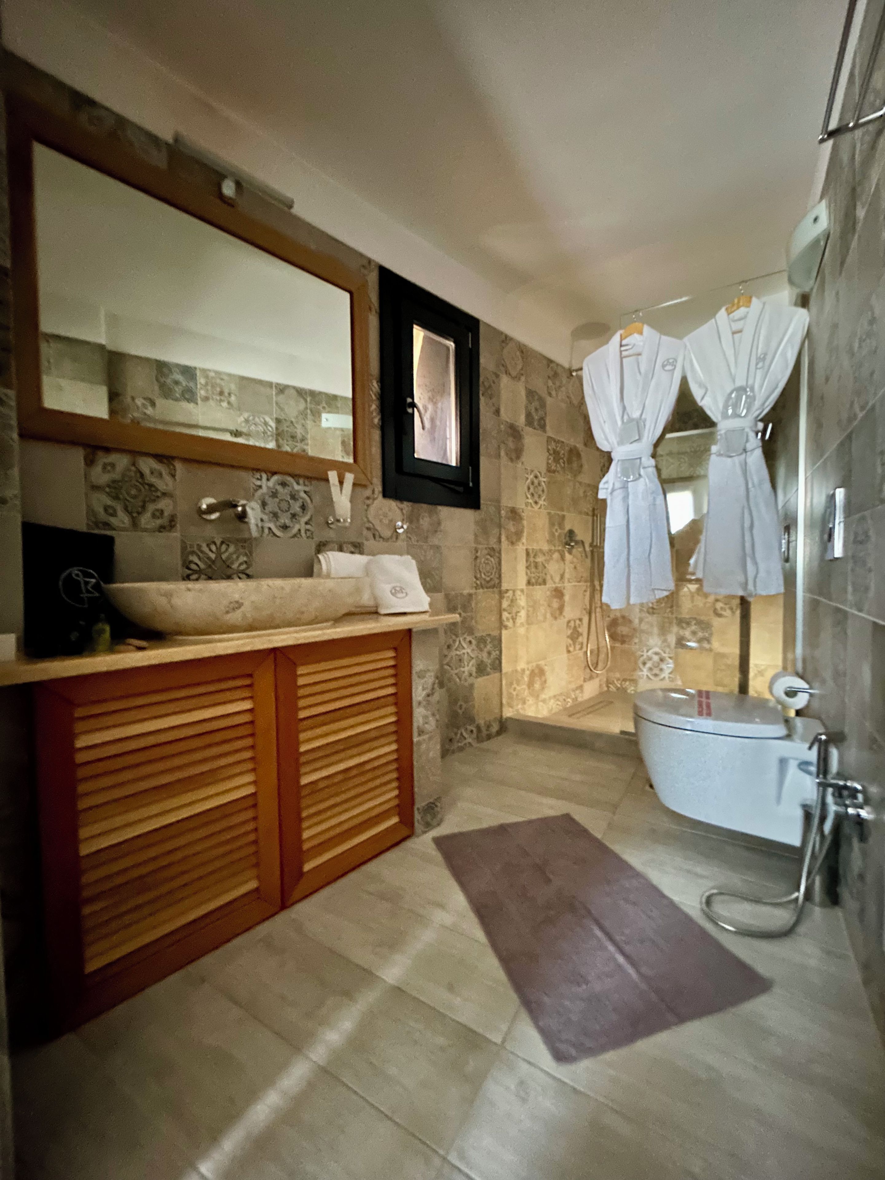 Une salle de bain avec un meuble-lavabo en bois, un grand miroir, une baignoire et deux serviettes suspendues à des crochets.