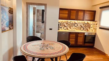 A compact kitchen with wooden cabinets, a tiled backsplash, and a dining area with a round table and chairs.