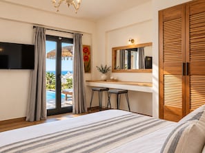 A bedroom with a large bed, a TV, a desk with two stools, a mirror, and a view of a pool and landscape.