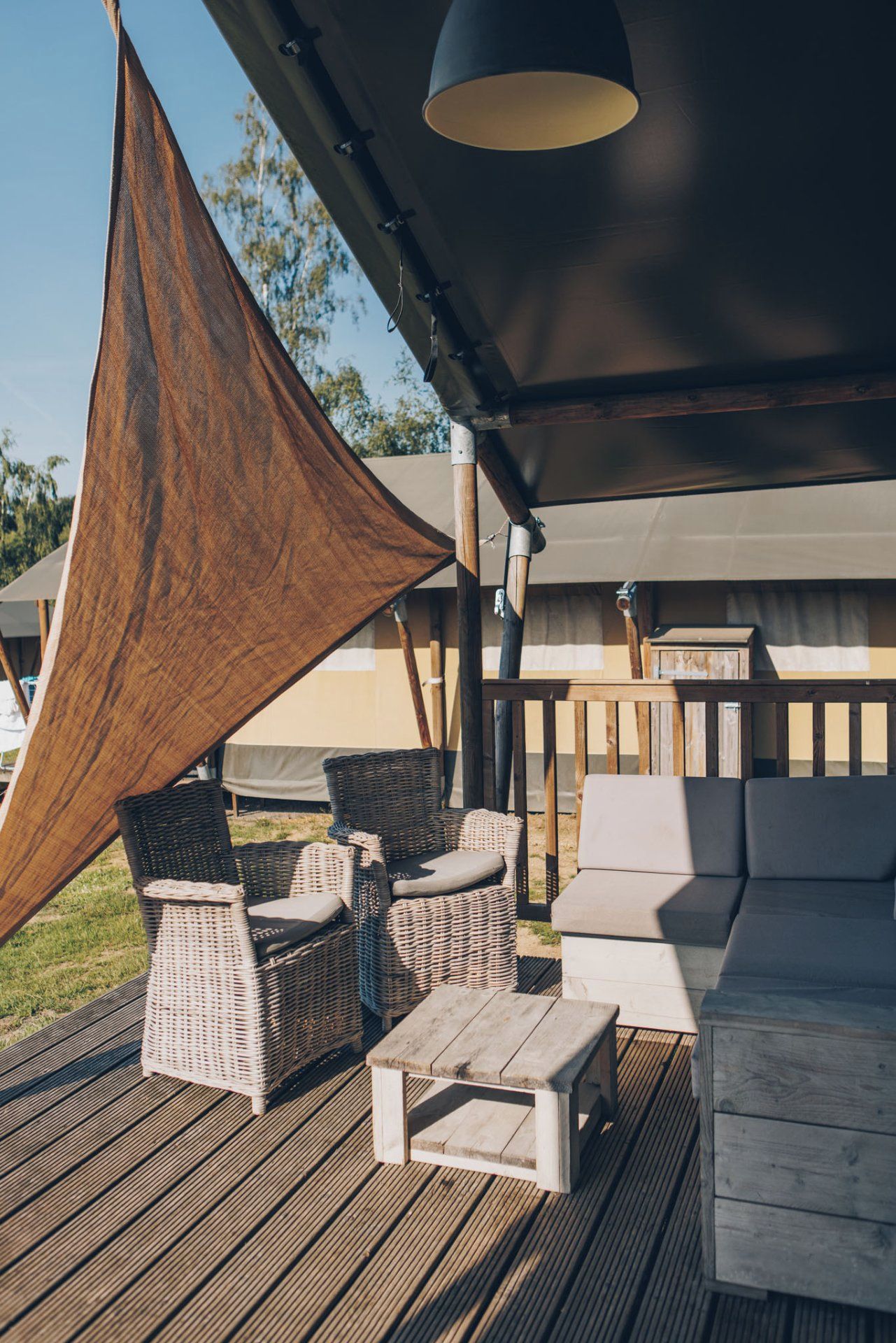 Eine Terrassenanlage im Freien mit Korbmöbeln, einem Holztisch und einem Sonnensegel.
