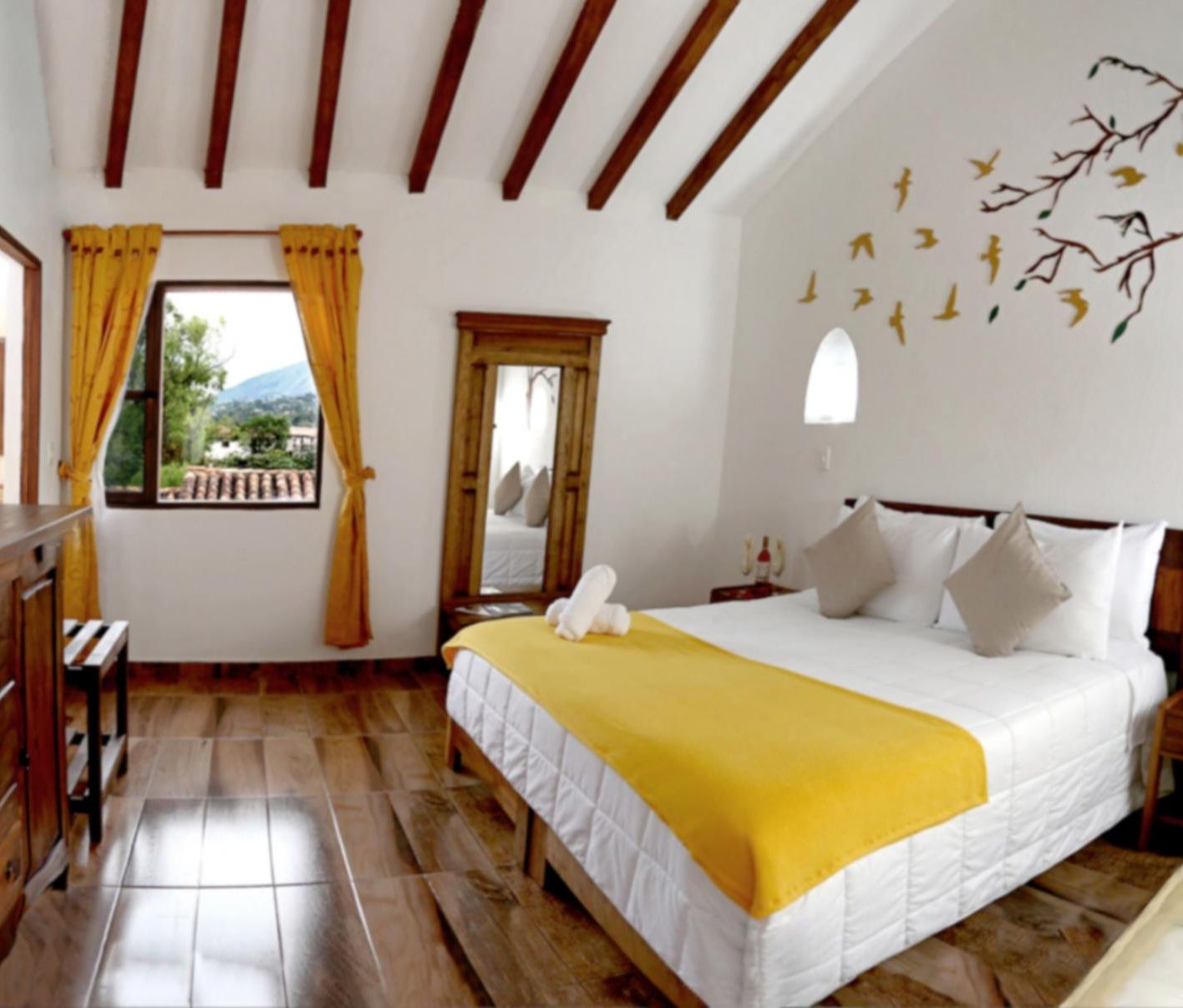 A hotel room with a bed, a window with curtains, a mirror, and a wall decoration of birds.