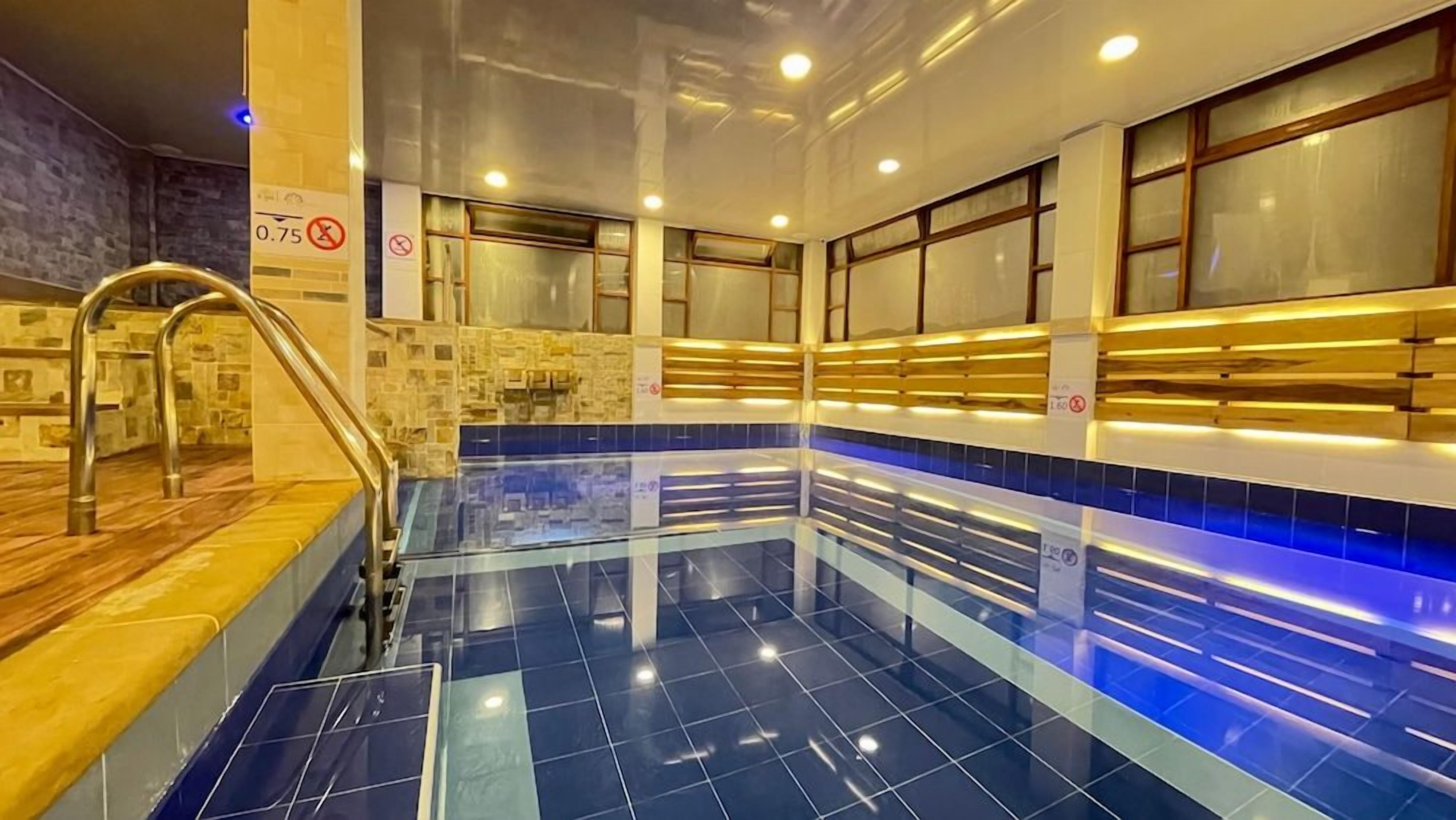 Une piscine avec un sol carrelé, un escalier en métal et une terrasse en bois.