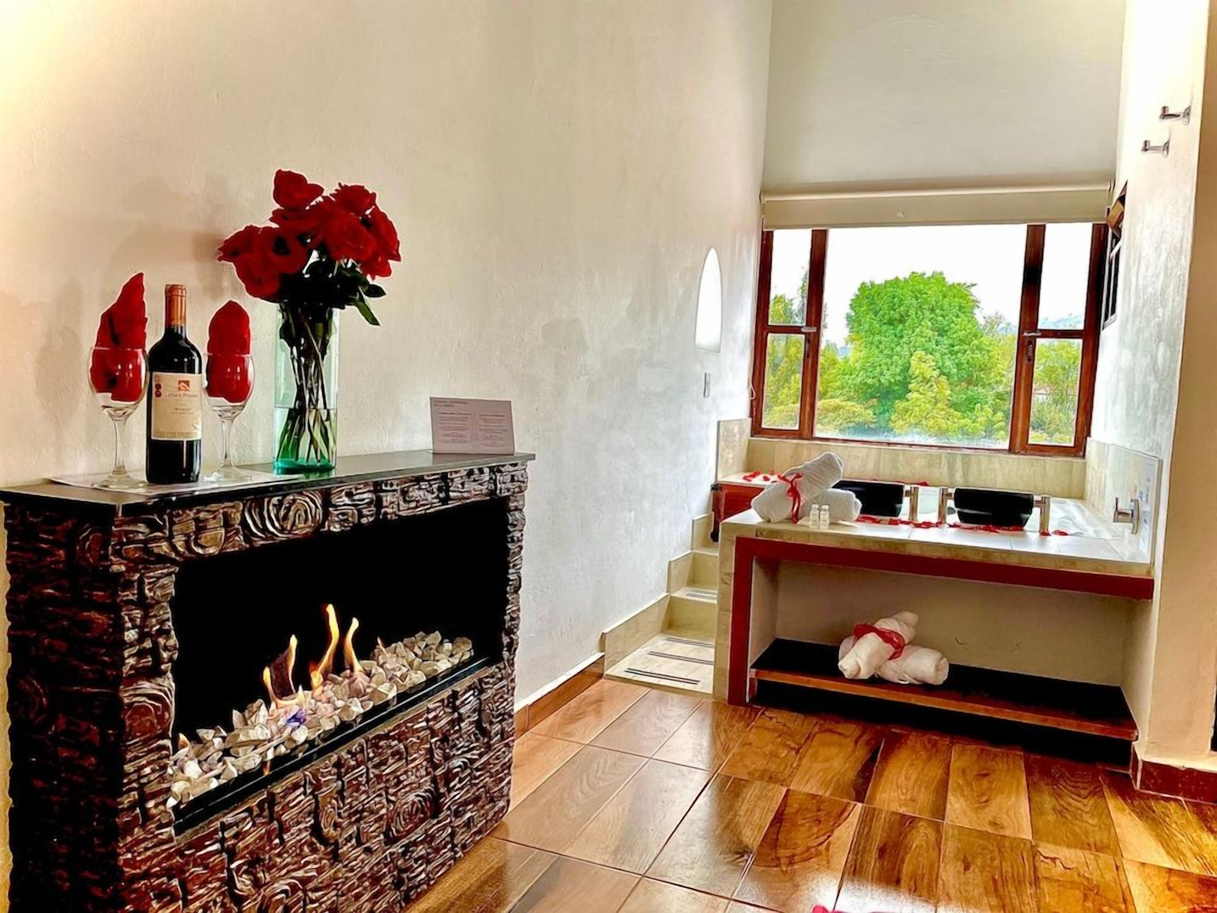 Une pièce avec une cheminée, une fenêtre donnant sur un beau paysage, un plancher en bois et une petite table sur laquelle est posé un vase de fleurs.