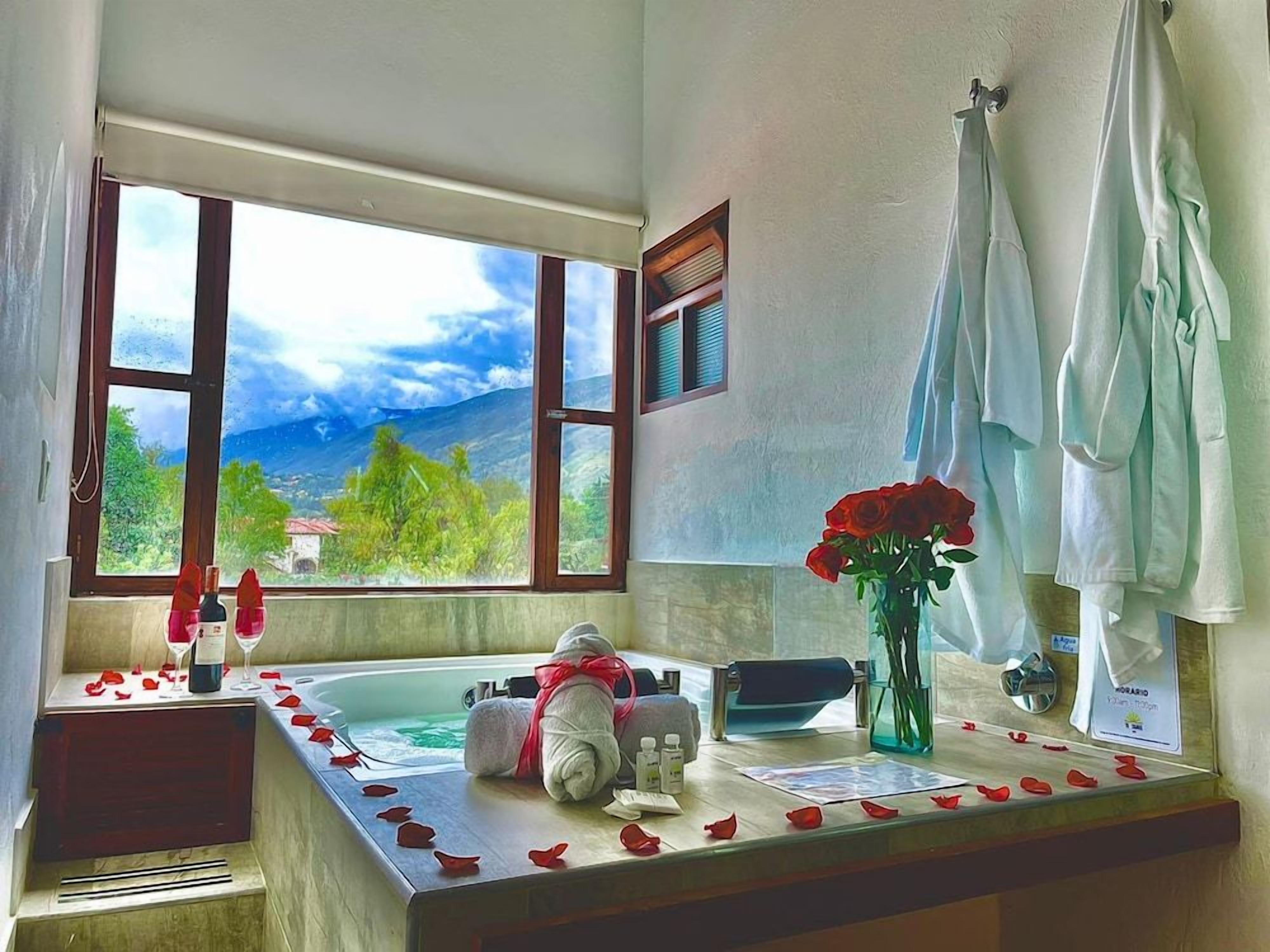 A bathroom with a bathtub, a window with a view of mountains, a vase with red roses, and towels.