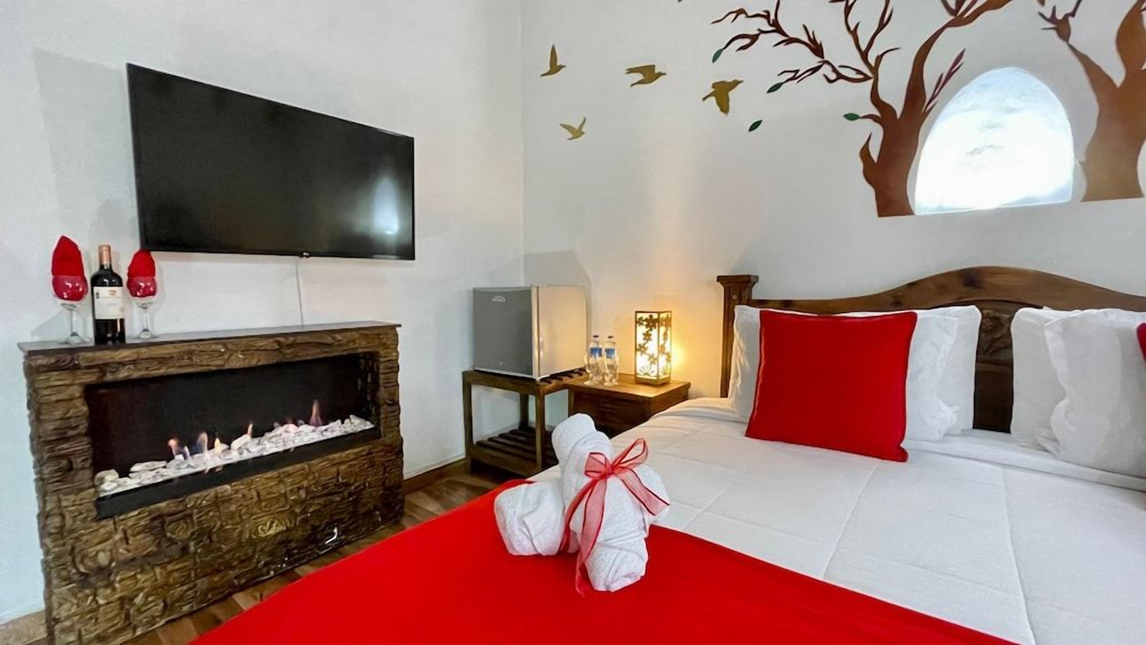 A hotel room with a fireplace, a flat-screen TV, a bed with red and white bedding, and a wall mural.