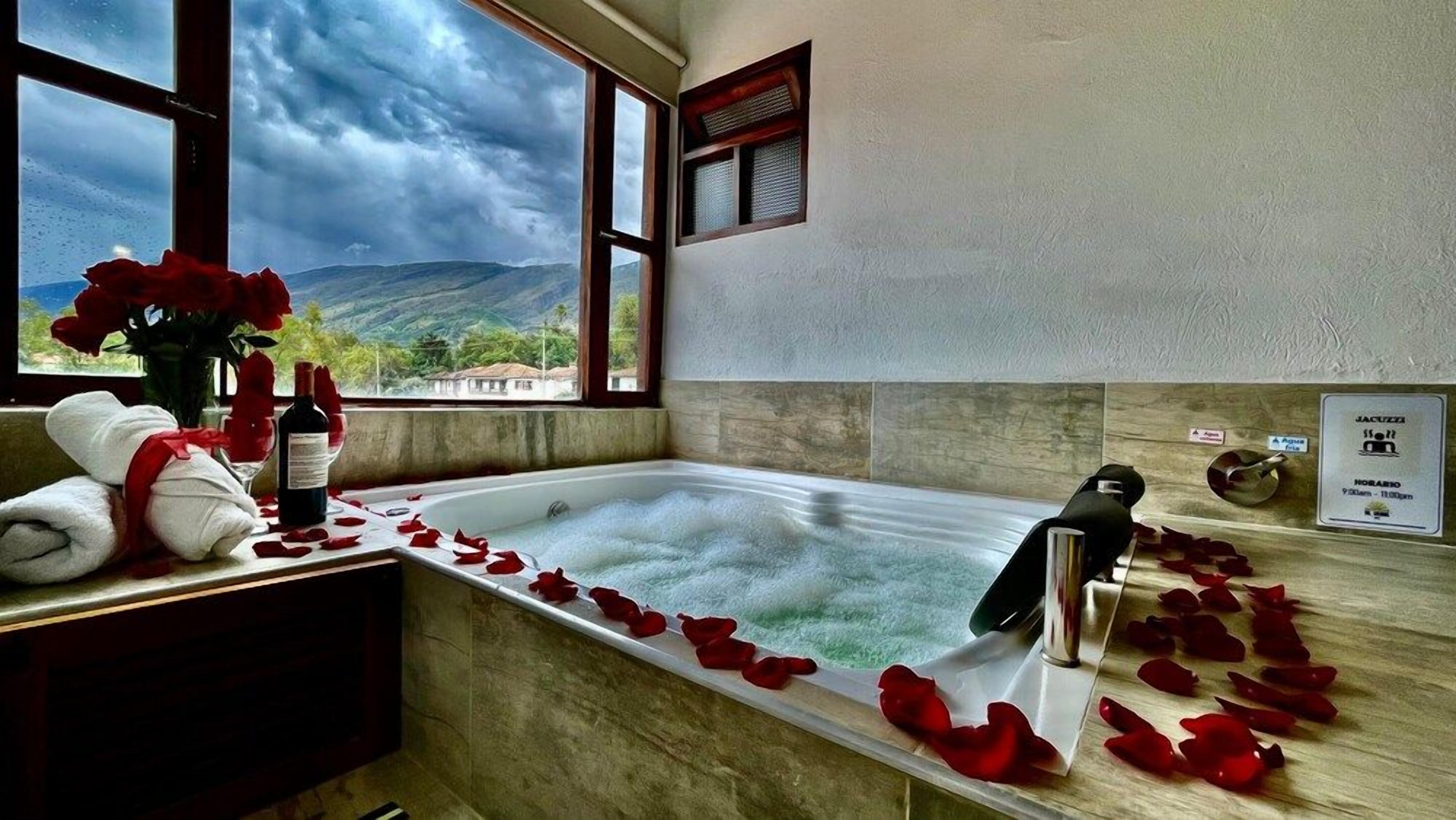 A bathroom with a bathtub, a window with a view of mountains, and rose petals on the floor.