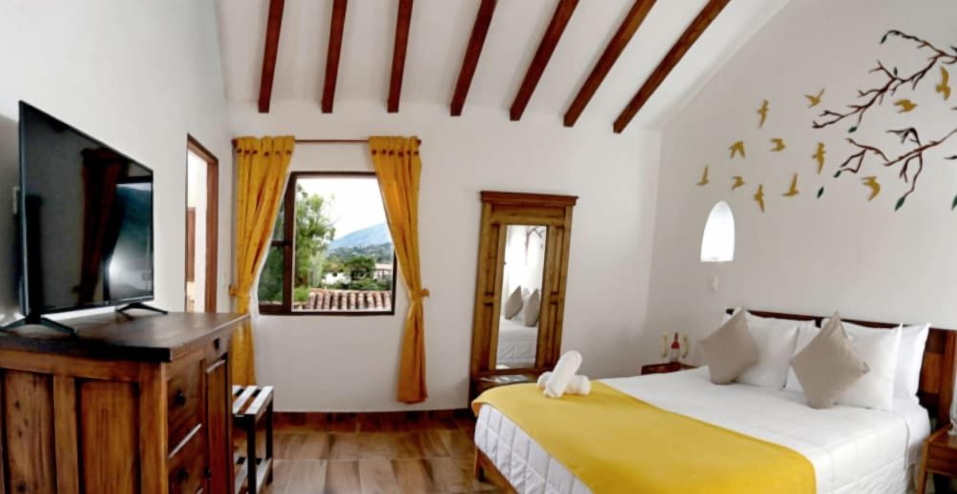 Un dormitorio con cama, televisor, ventana con cortinas, espejo y decoración en la pared.