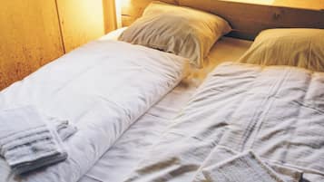 A single bed with a headboard, a window with blinds, and a towel on the bed.