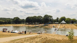 Un parc a la vora d'un llac amb zones de sorra, una rampa per a embarcacions i un edifici petit.