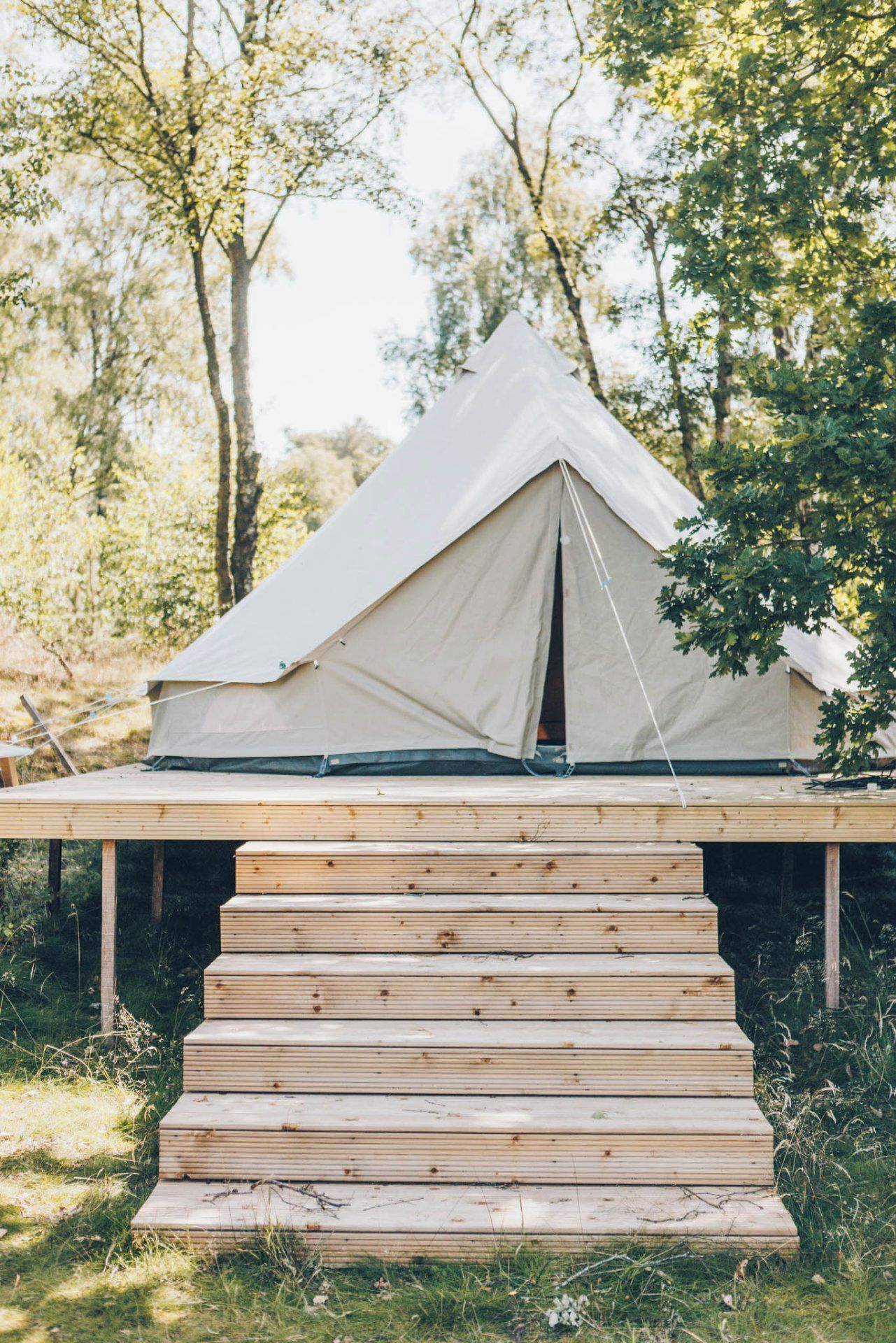 A tent set up on a wooden platform in a wooded area.