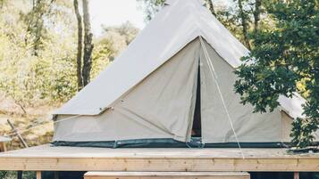 A tent set up on a wooden platform in a wooded area.