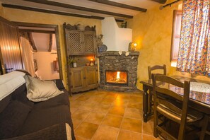 Ein gemütliches Wohnzimmer mit Kamin aus Stein, Holzmöbeln und Fliesenboden.