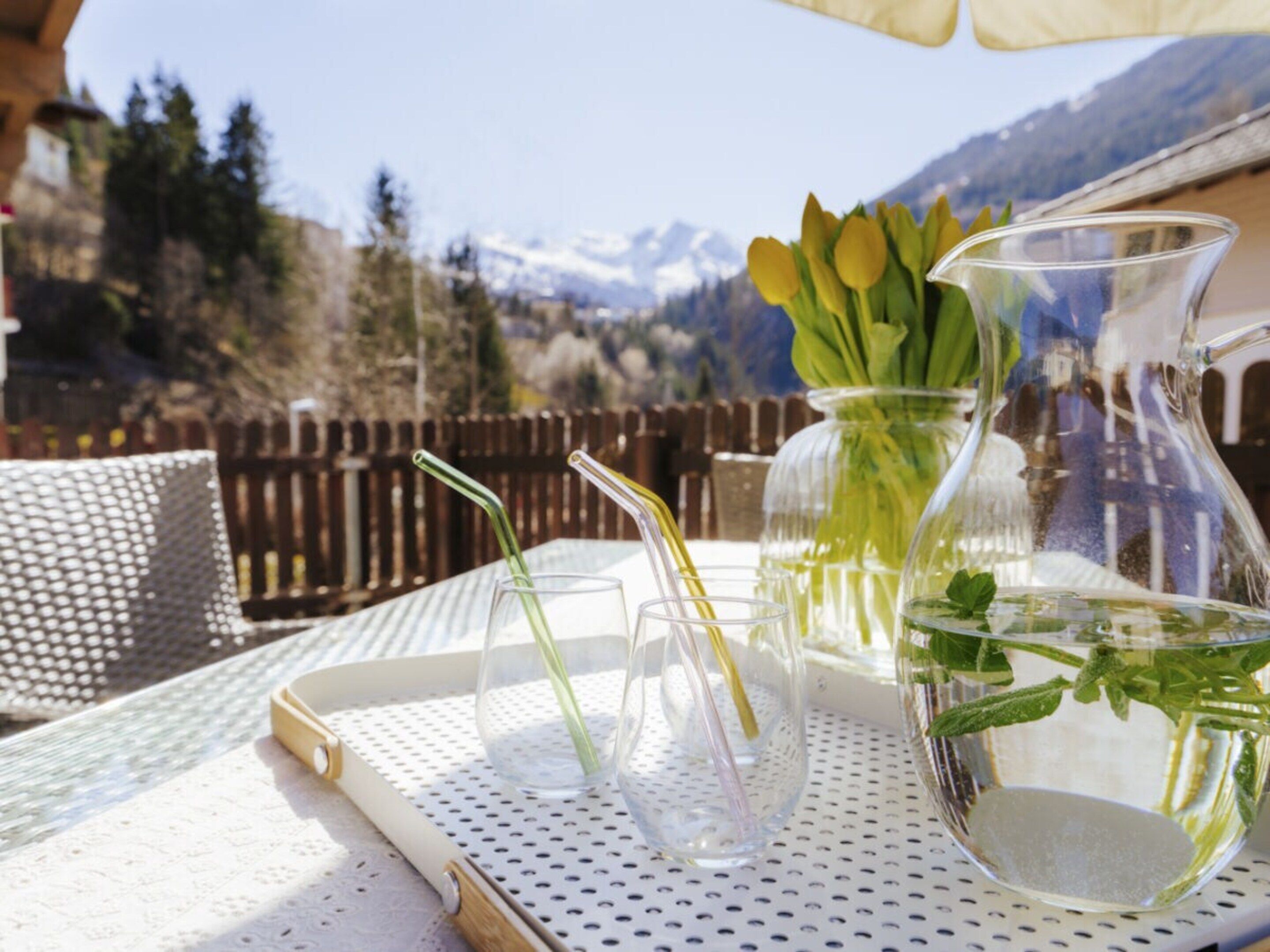 A table with a pitcher, glasses, and a tray, set outdoors with a mountain view.