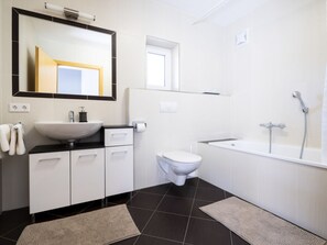 A modern bathroom with a white sink, toilet, and bathtub. There are two rugs on the floor. - Holiday Home With 3 Bedrooms (Bad Gastein)