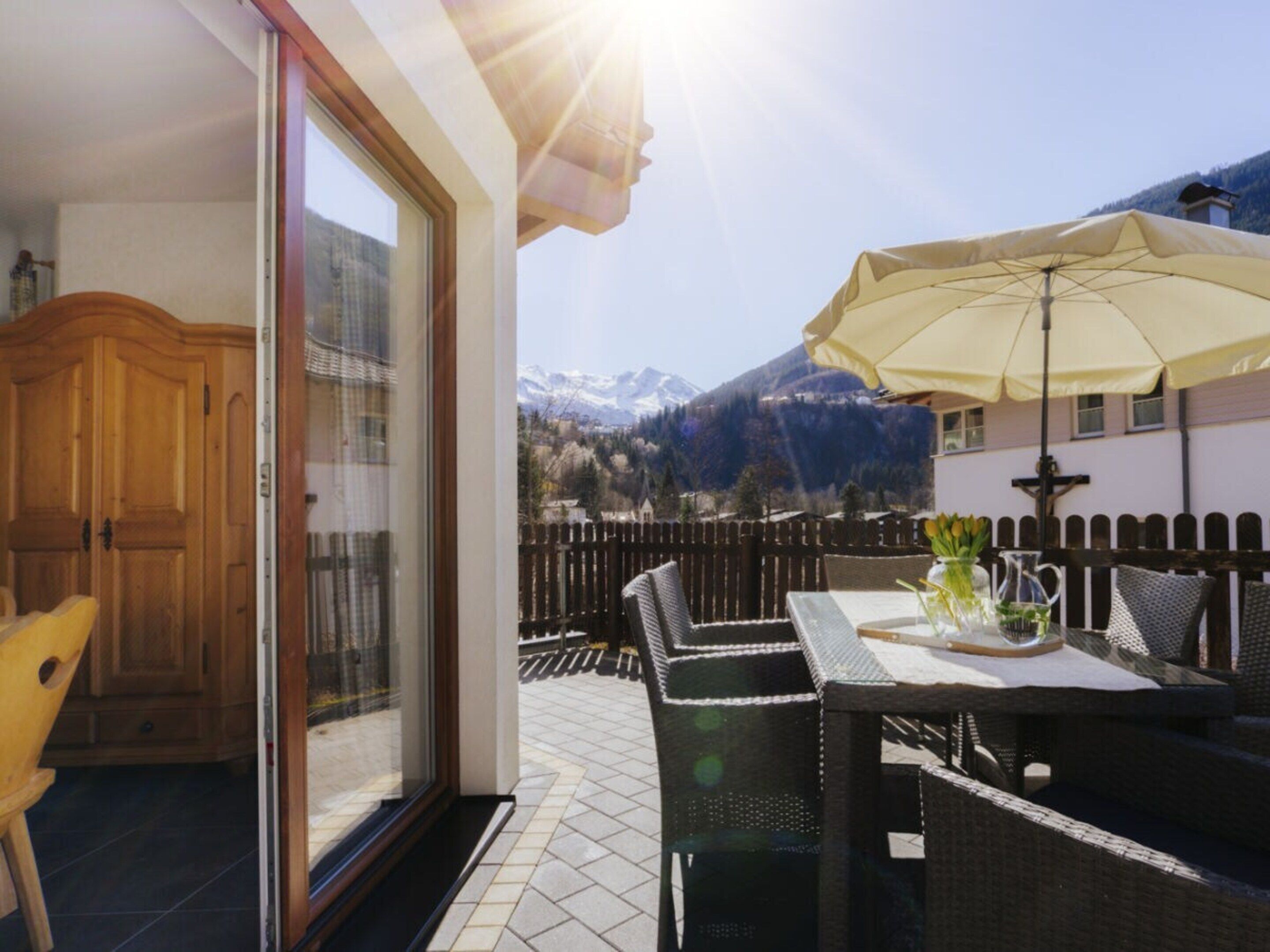 A balcony with a table and chairs, a wooden door, and a view of mountains.