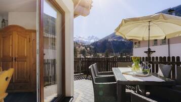 A balcony with a table and chairs, a wooden door, and a view of mountains.