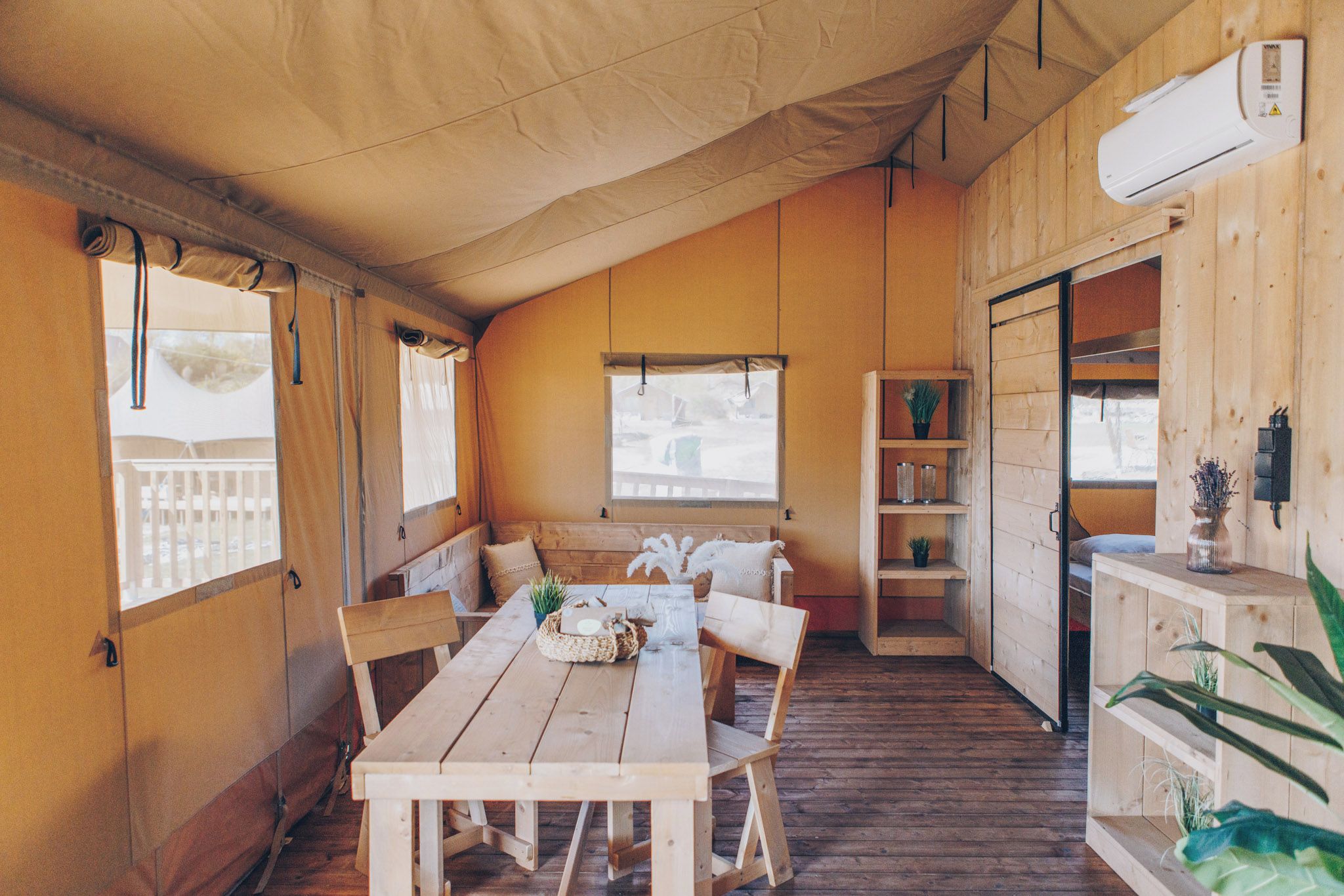 Una tenda arredata con un tavolo e sedie in legno, una finestra con tende e uno scaffale con oggetti decorativi.