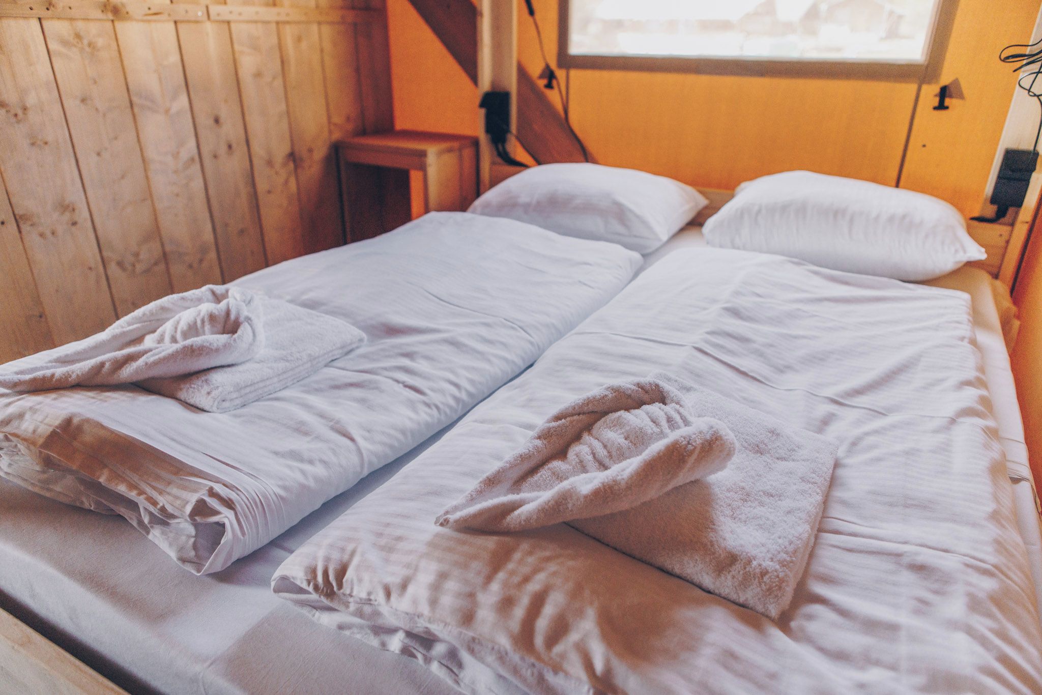 Ein Doppelbett mit weißen Bettwäsche und Handtüchern, Holzwände und ein kleiner Nachttisch.