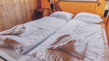 A double bed with white linens and towels, wooden walls, and a small bedside table.