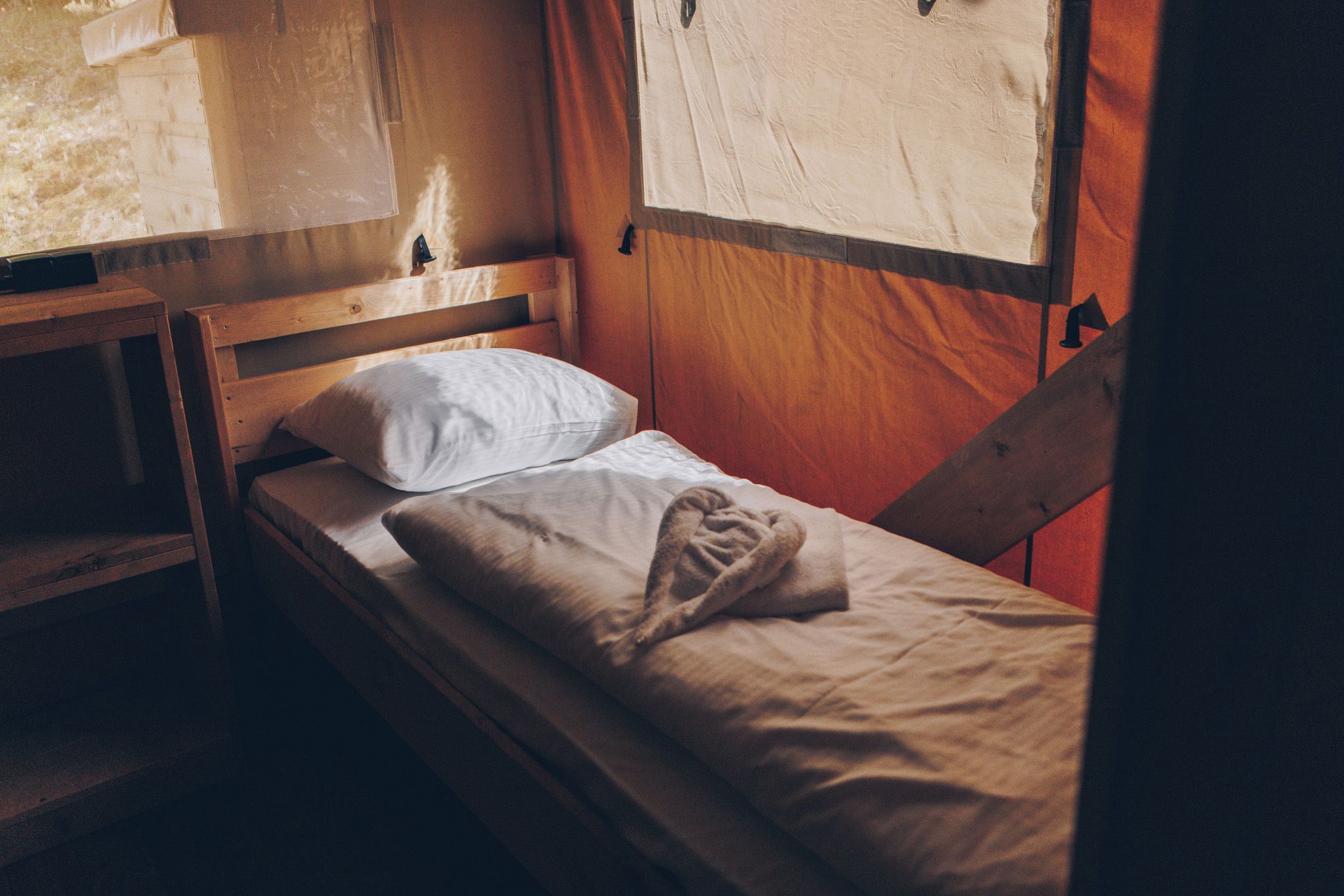 Un lit simple avec une tête de lit en bois, un oreiller blanc et une couverture beige.