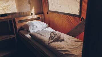 Un lit simple avec une tête de lit en bois, un oreiller blanc et une couverture beige.