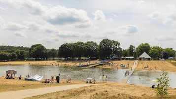 En park ved søen med sandstrande, en bådebro og en mindre bygning.
