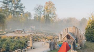Ein Spielplatz mit einer Holzspielkonstruktion, einer roten Kletterwand und einem Picknicktisch in einer Parkanlage.