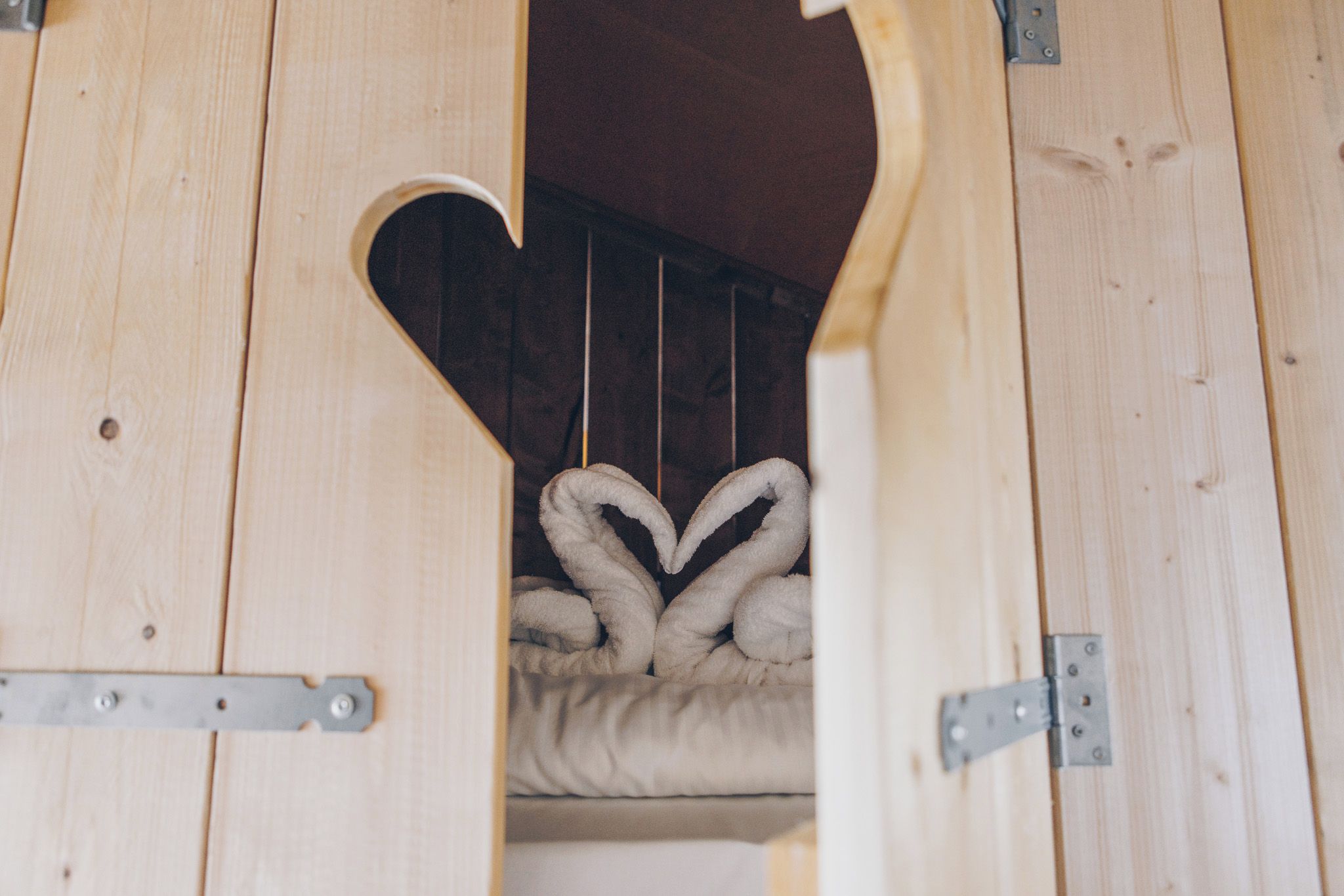 Una estructura de madera con una abertura en forma de corazón, que muestra una cama con una manta blanca.