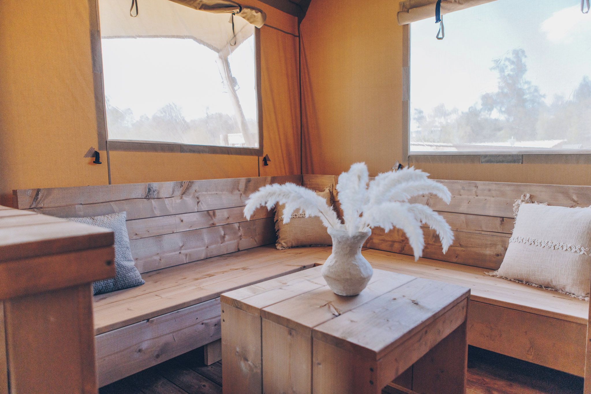 Ein gemütliches Cabin-Interieur mit einer Holzbank, einem kleinen Tisch mit einer Vase voller weißer Federn und einem Fenster mit Blick auf Bäume.