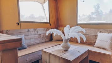 Ein gemütliches Cabin-Interieur mit einer Holzbank, einem kleinen Tisch mit einer Vase voller weißer Federn und einem Fenster mit Blick auf Bäume.