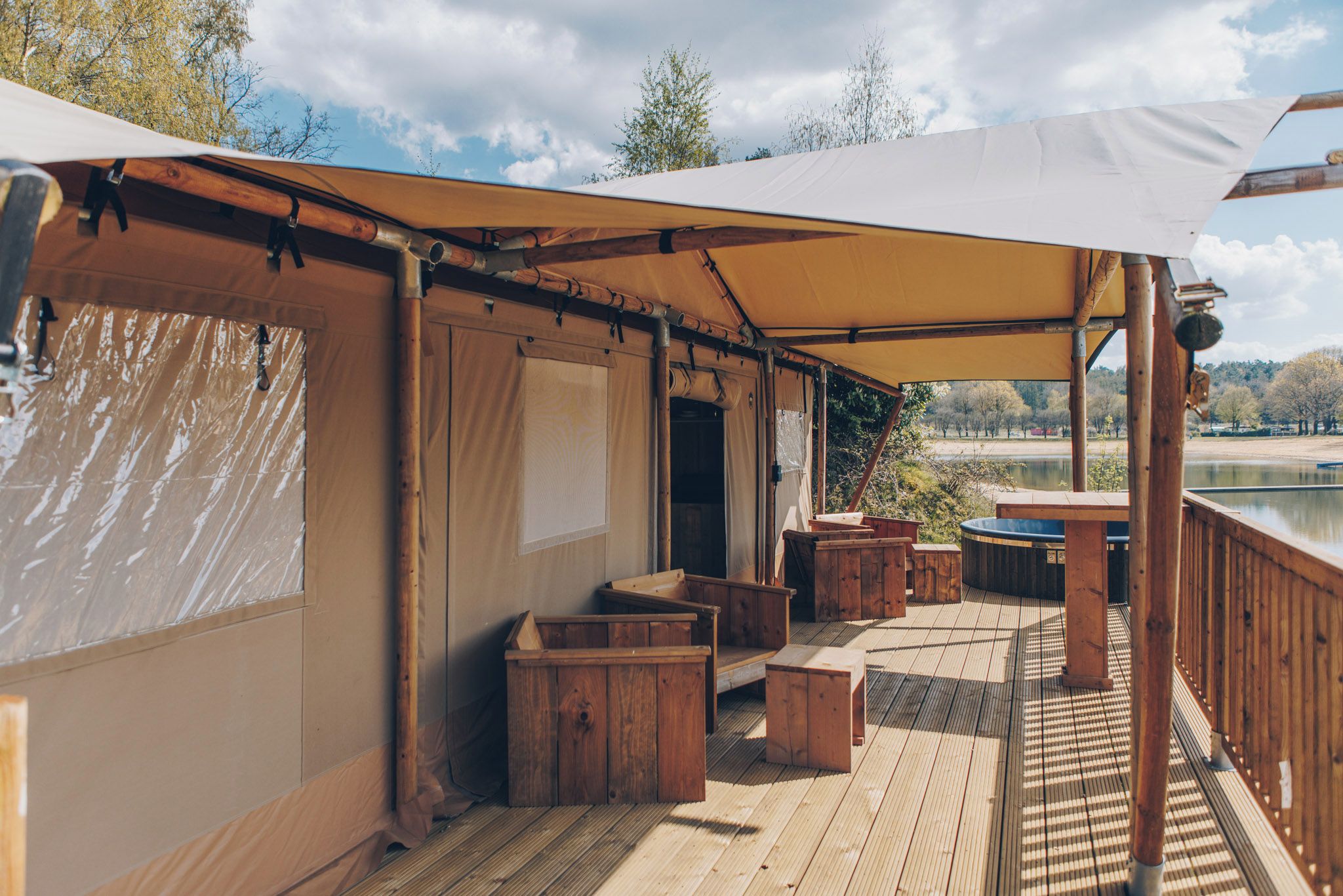 En overdækket terrasse med træmøbler og udsigt til en sø.