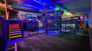 Un espace de jeux avec un toboggan en spirale, une structure d’escalade à plusieurs niveaux et un escalier coloré.