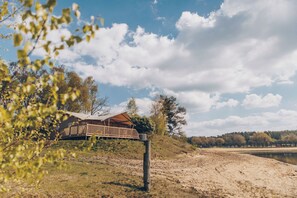 A wooden cabin with a deck, surrounded by trees and a clear sky.