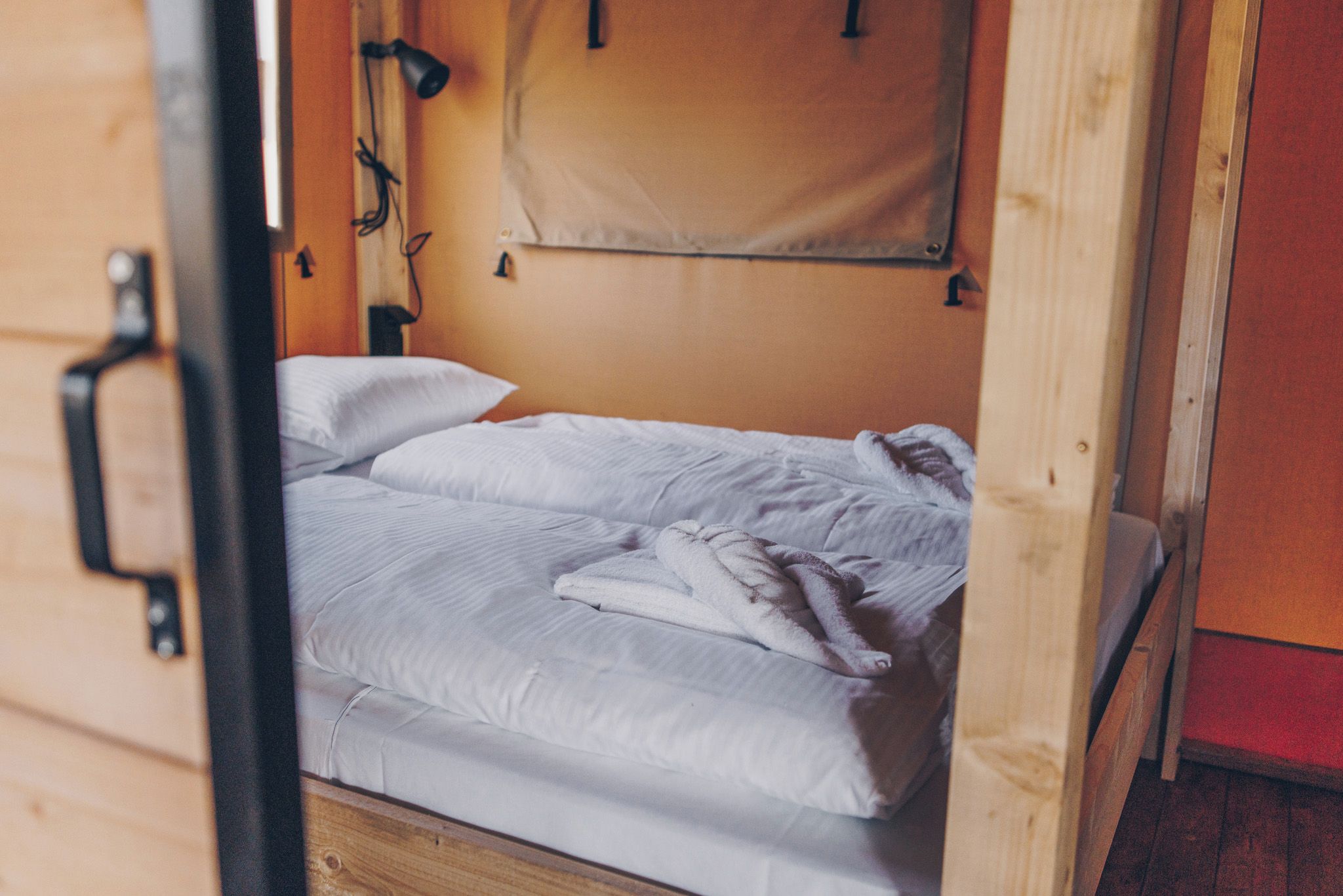 Ein Einzelbett mit weißer Bettwäsche in einem Zimmer mit Holzwänden und einer Holztür.