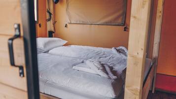 Ein Einzelbett mit weißer Bettwäsche in einem Zimmer mit Holzwänden und einer Holztür.
