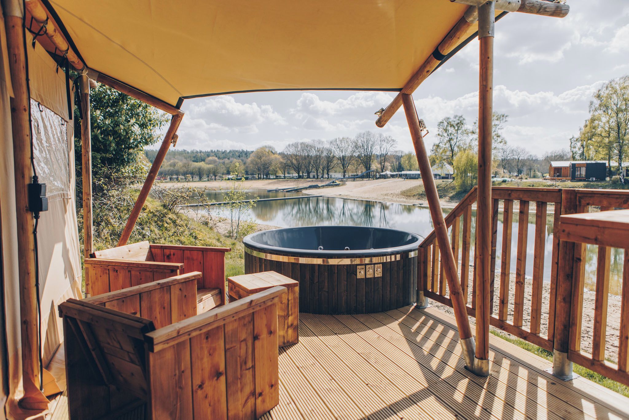 Eine Holzterrasse mit Whirlpool, Holzliegen und Blick auf einen See und Bäume.