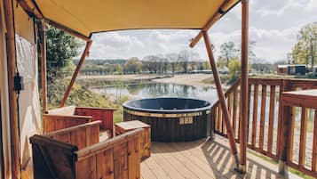 Eine Holzterrasse mit Whirlpool, Holzliegen und Blick auf einen See und Bäume.