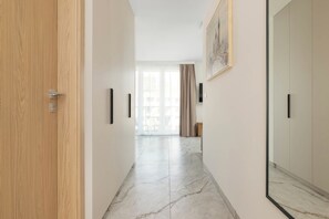 A hallway with a wooden door, a mirror, and a view into a room with a large window and curtains. - Cracow | Łaszkiewicza 8B | Comfortable Apartment | Parking (Kraków)