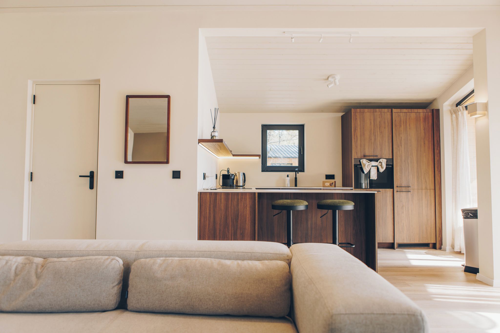 A modern living room with a sectional sofa and a kitchen area with wooden cabinets and a stainless steel refrigerator.