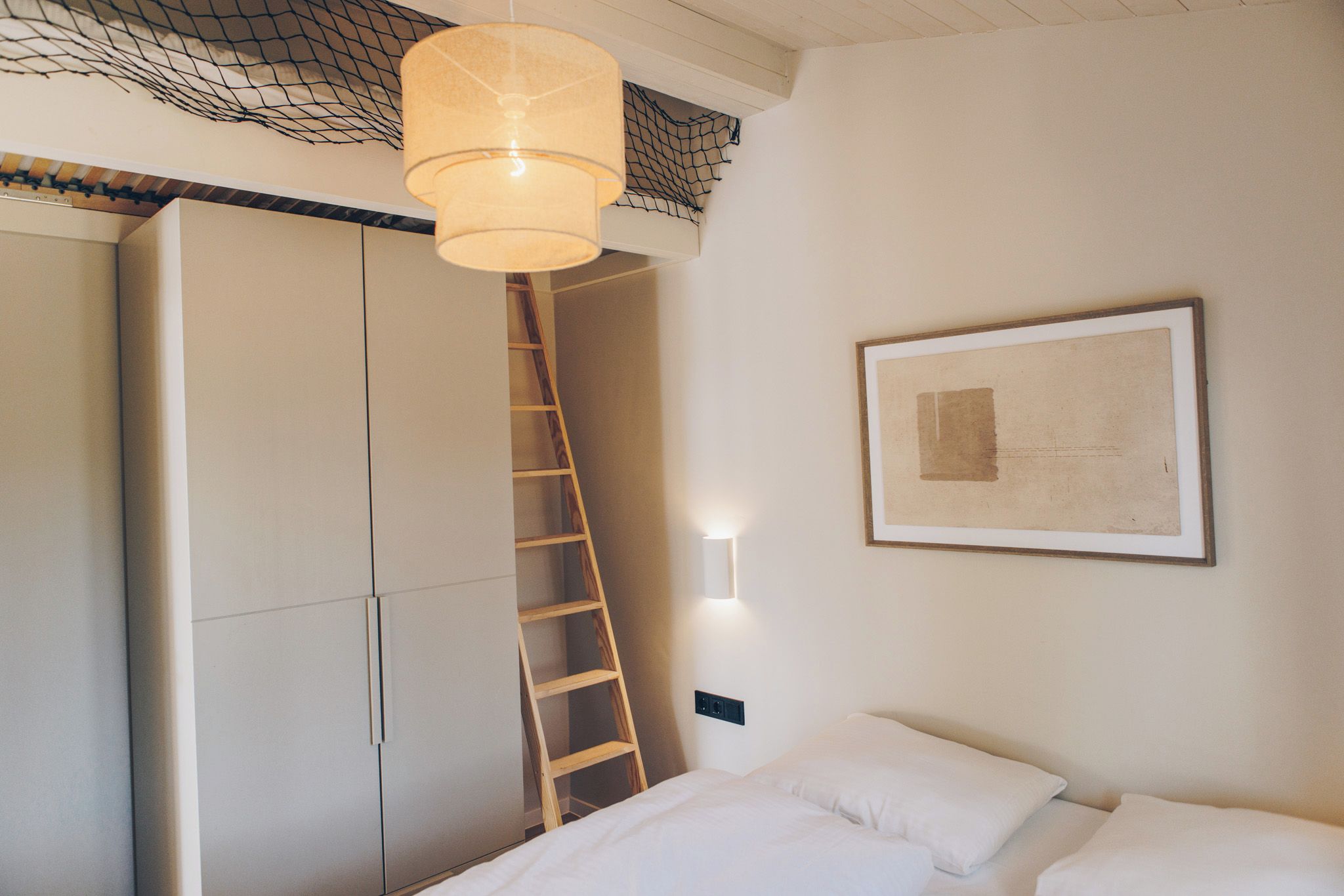 A bedroom with a bed, a ladder, a wardrobe, and a wall-mounted light fixture.