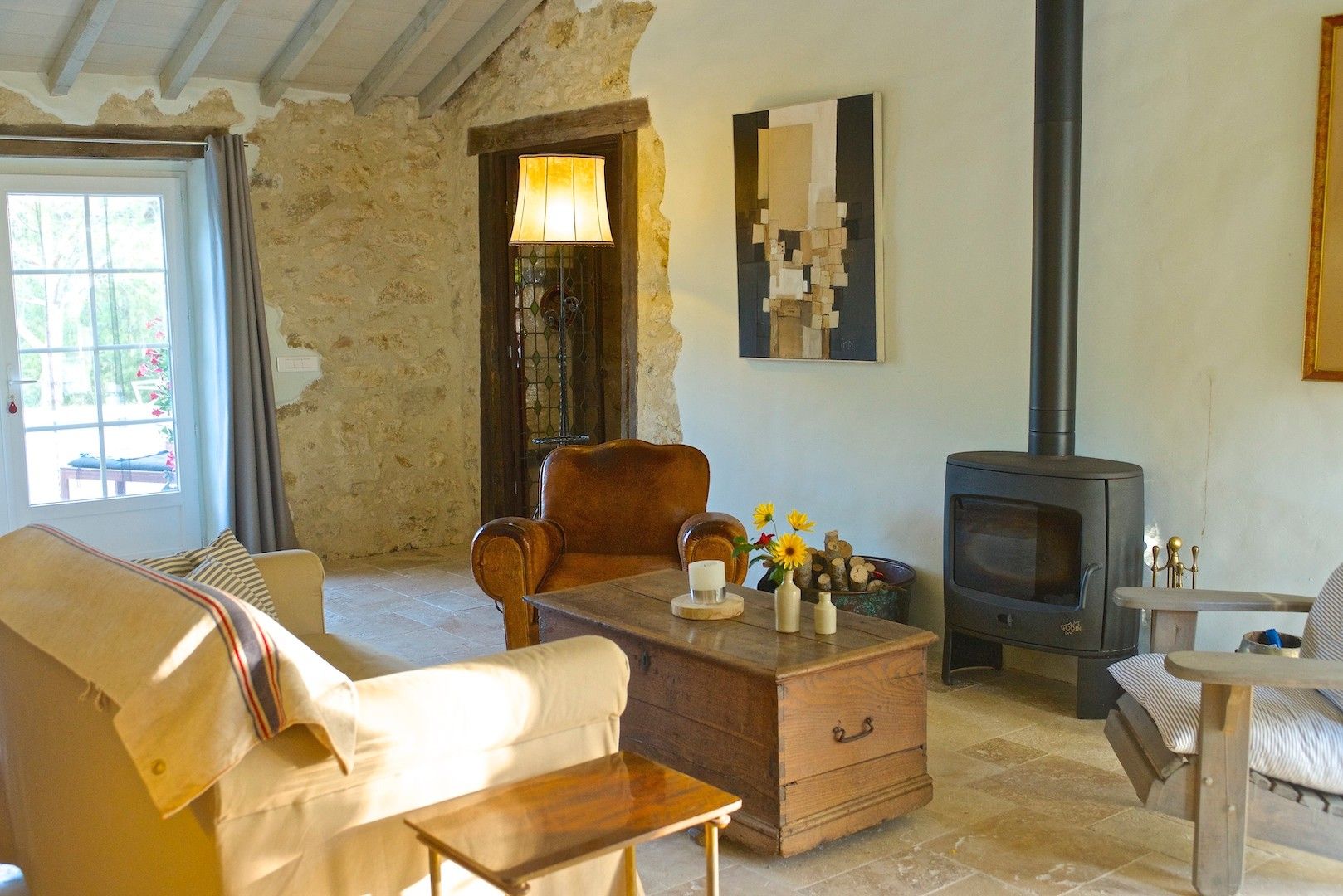 Una sala de estar rústica con pared de piedra, un sofá de madera, un sillón de cuero, una mesa de centro de madera, una chimenea y una ventana con cortinas.