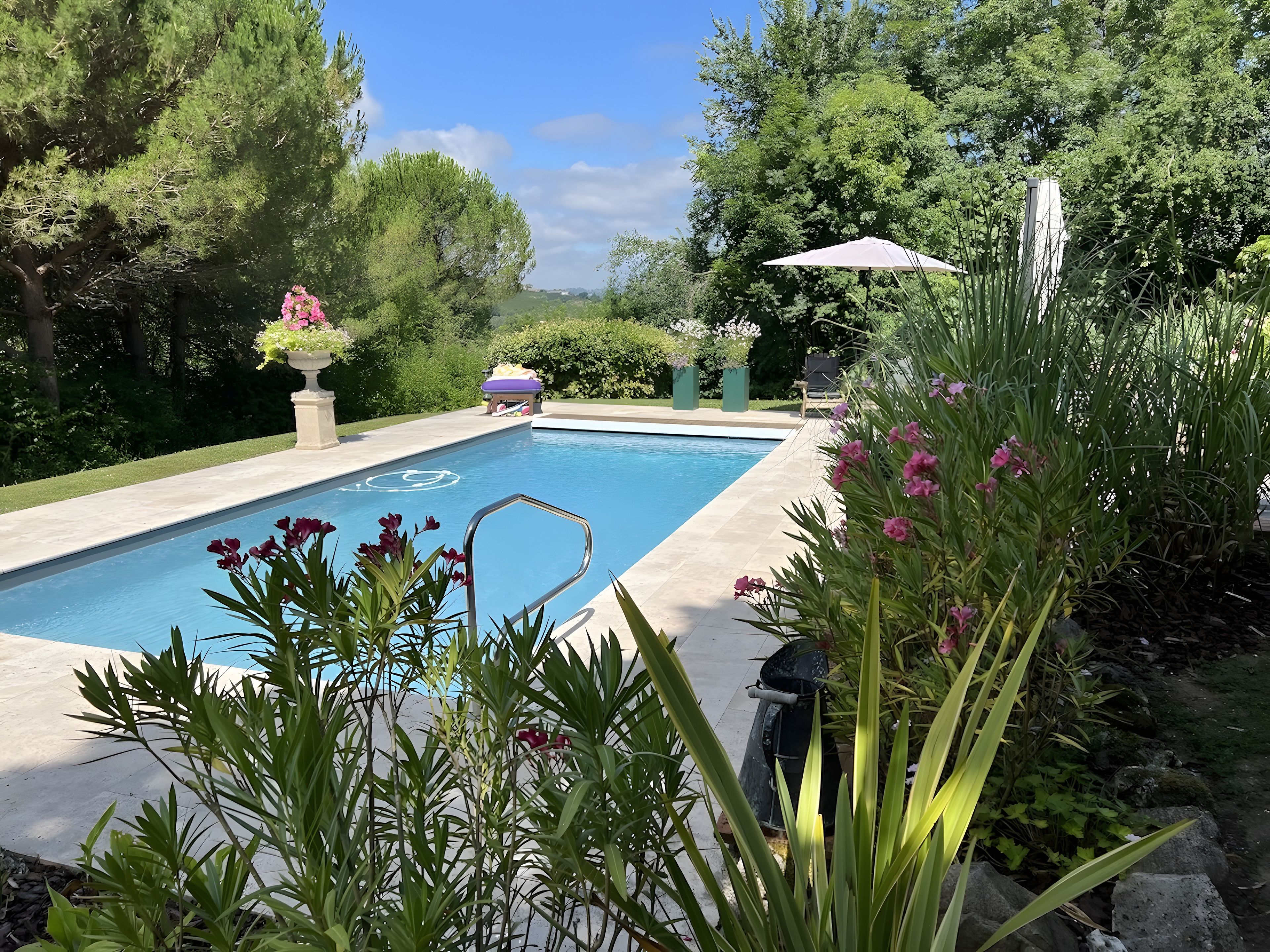 En swimmingpool med tilhørende have, liggestol og parasol.