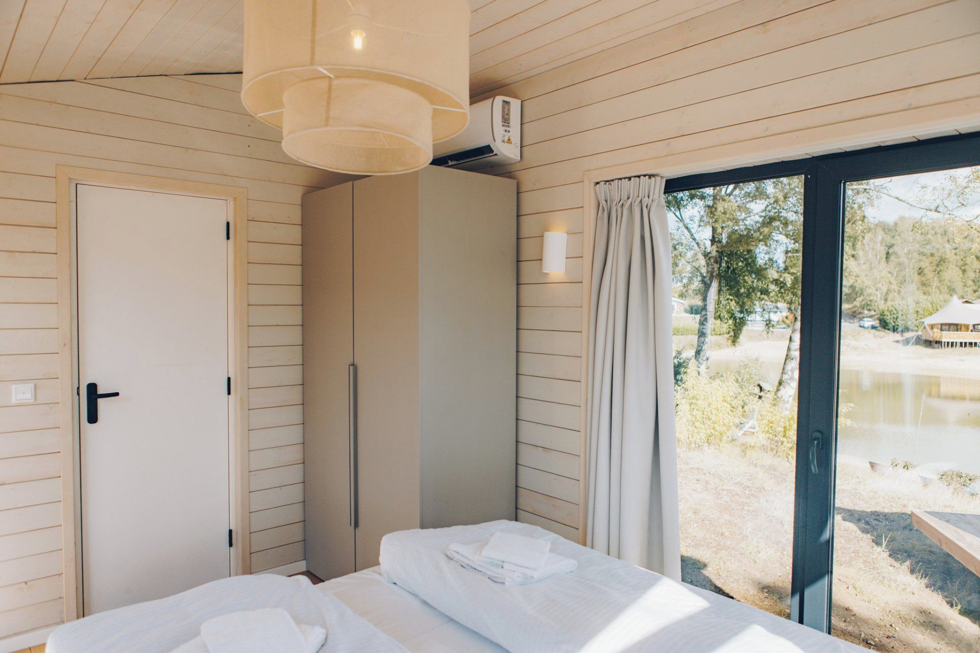 Ein Schlafzimmer mit Bett, Kleiderschrank, einem Fenster mit Vorhängen und einer Deckenleuchte.