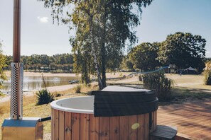 A hot tub on a wooden deck with a view of a lake and trees.