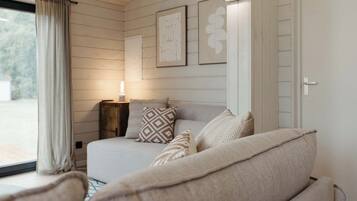 Une chambre à coucher avec un lit, des oreillers, une table de chevet et une lampe. Des tableaux encadrés ornent le mur, et il y a une fenêtre avec des rideaux.